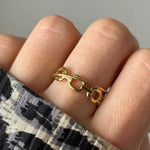 Bague dorée à maillons de chaîne ronds lisses sur un doigt, avec une fine bande dorée finement texturée. Tissu imprimé animal.