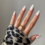 Main féminine avec bague dorée à maillons sur l'annulaire. Ongles longs ovales laiteux. Manchette imprimé léopard.