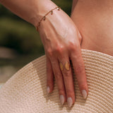 Bague ouverte en acier inoxydable doré motif coquillage sur main et chapeau de paille.