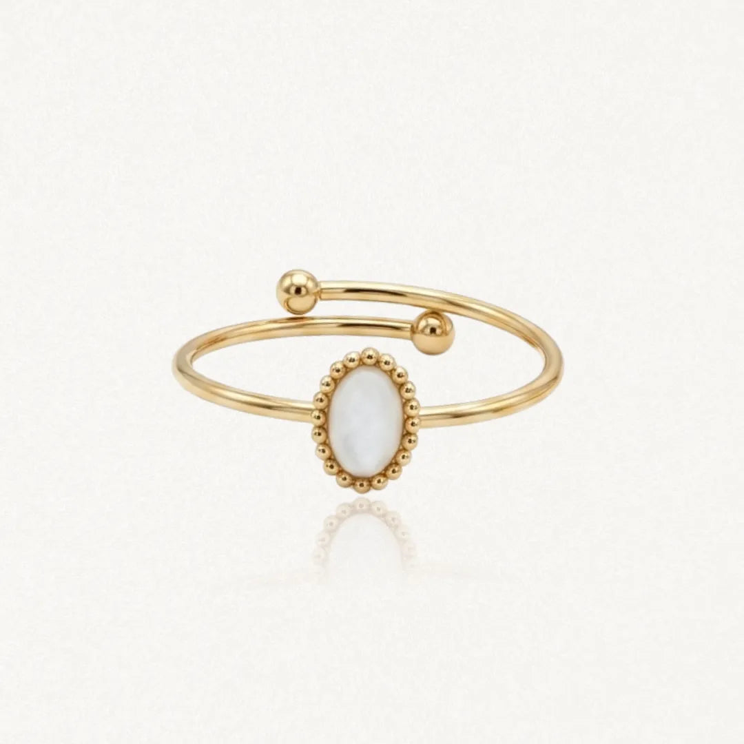 Bague ouverte dorée avec un insert ovale blanc nacré entouré de petites perles dorées et deux boules aux extrémités.