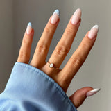 Main portant une bague fine dorée avec nacre ovale. Ongles longs style French manucure à pois et bouts colorés sur manche
