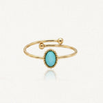 Bague dorée ouverte avec pierre ovale turquoise entourée de perles. Deux boules dorées terminent l'anneau.