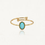 Bague dorée ouverte avec pierre ovale turquoise entourée de perles. Deux boules dorées terminent l'anneau.