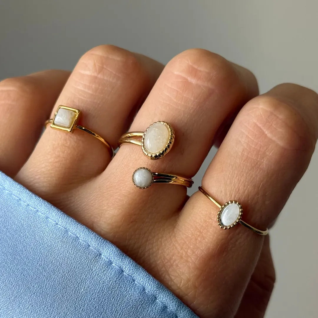 Gros plan sur une main portant quatre bagues dorées. Les pierres, blanches et opalescentes, sont carrées, ovales ou rondes.