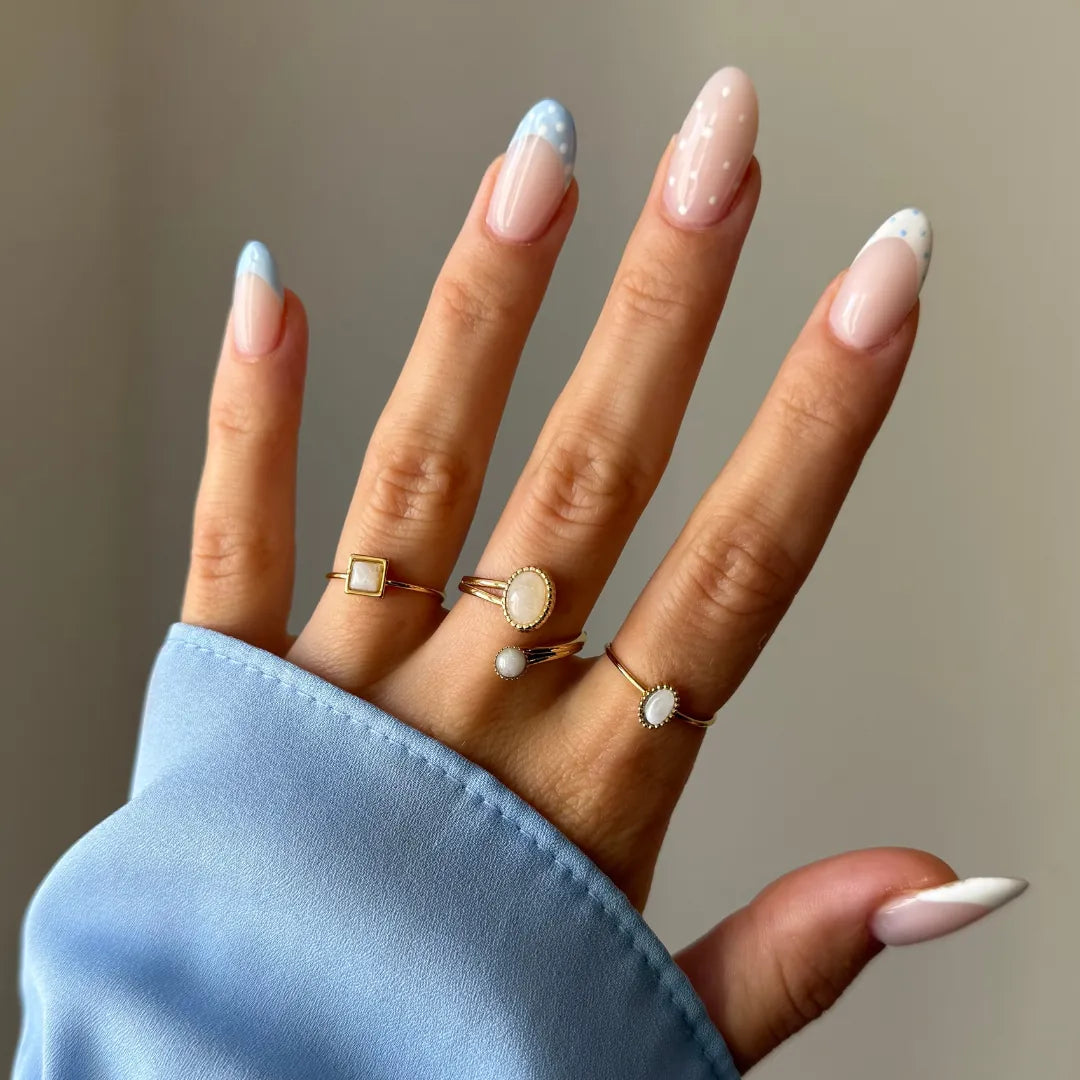 Main de femme avec 4 bagues dorées et pierres nacrées blanches. Une carrée, deux ovales et une avec perle. Ongles décorés,