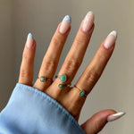 Quatre bagues dorées avec des pierres turquoise ovales et carrées sur une main aux ongles manucurés.