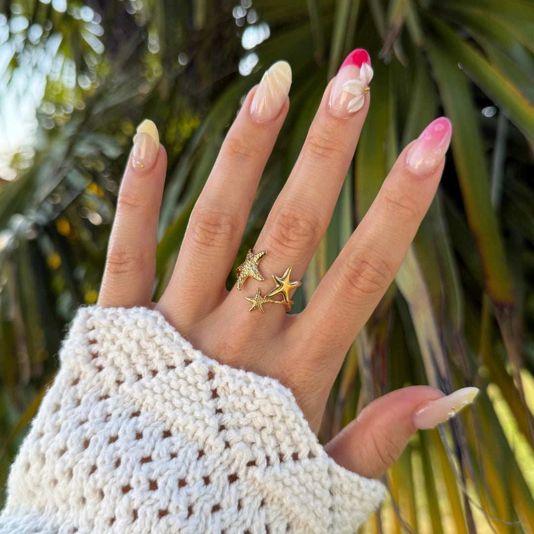 Bague en acier inoxydable doré, motif étoiles et étoile de mer pavée, sur main avec manchette en tricot blanc.