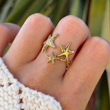 Bague en acier inoxydable doré, motif 3 étoiles de mer texturées de tailles variées sur un doigt de femme.