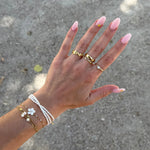 Bague large ondulee en acier inoxydable dore de 0,9 cm de haut, portee sur l'index d'une main feminine.
