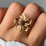 Bague fleur en acier inoxydable doré portée au doigt. La fleur ajourée a des pétales martelés et un centre texturé.