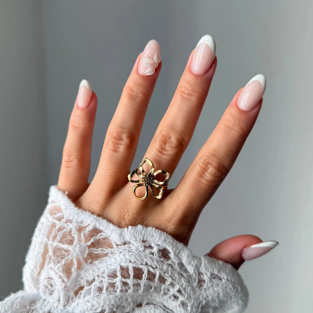Main portant une bague ajustable en acier inoxydable doré, au design ajouré en forme de fleur avec un centre foncé, sur un