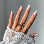 Main portant une bague ajustable en acier inoxydable doré, au design ajouré en forme de fleur avec un centre foncé, sur un