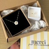 Dans une boîte cartonnée, une bague en acier inoxydable dore ornée d'une fleur en nacre, et un collier à perles assorti.