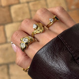 Bague GIGI en acier inoxydable doré avec strass en zirconium sur une main portant plusieurs bagues