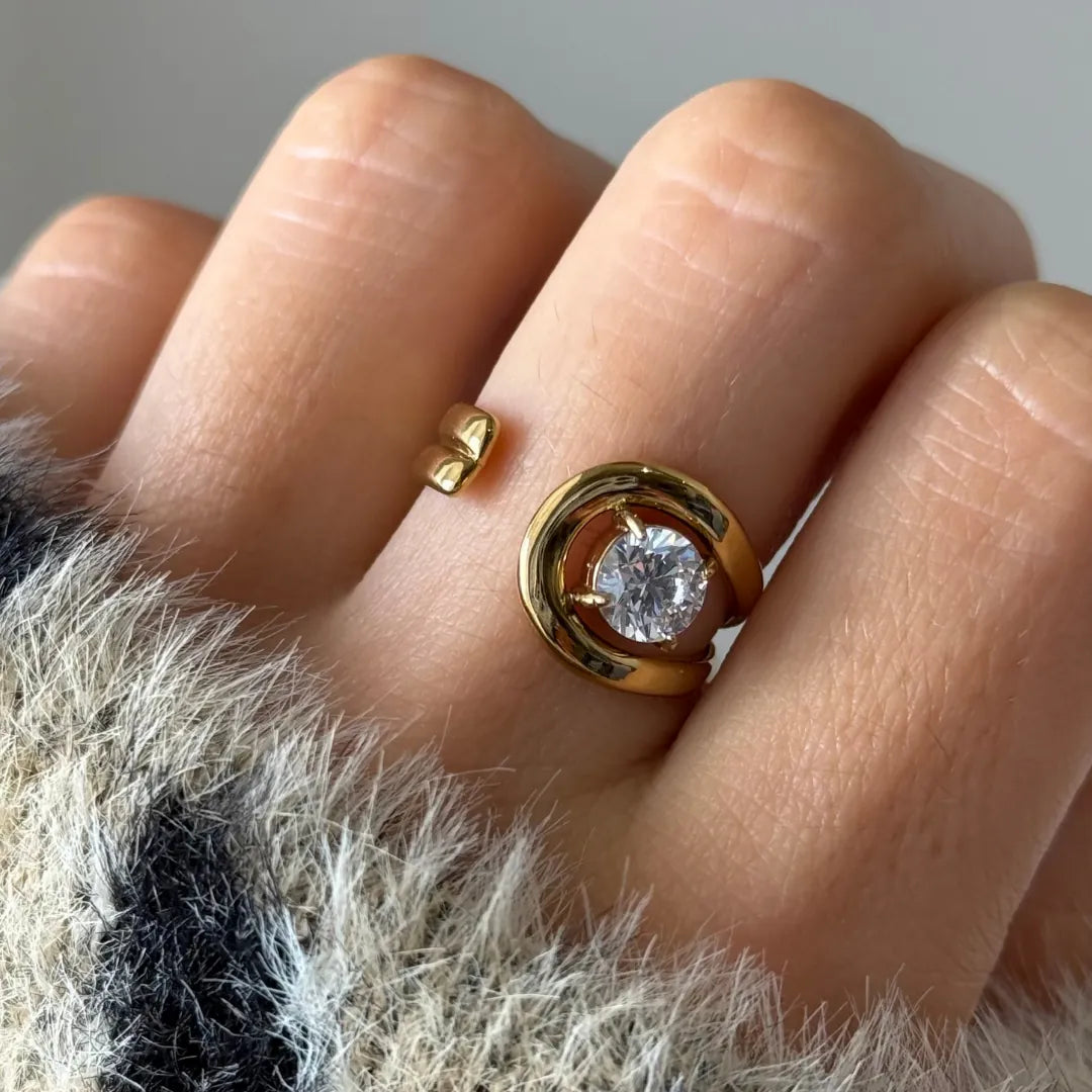 Bague spirale ouverte en acier inoxydable doré avec zirconium rond, portée sur un doigt.