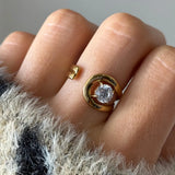 Bague spirale ouverte en acier inoxydable doré avec zirconium rond, portée sur un doigt.