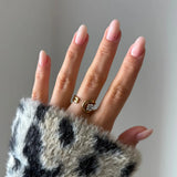 Bague spirale en acier inoxydable doré et zirconium rond portée sur une main aux ongles roses, avec une manche pelucheuse à