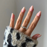 Main aux ongles roses portant une bague demi-alliance en acier inoxydable doré avec cinq zircons ronds.