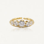 Bague ajustable en acier inoxydable doré, ornée de cinq zircons ronds, le central étant plus grand. Bande texturée.