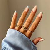 Main féminine au chemisier bleu clair, parée de trois bagues en acier inoxydable doré avec des ornements. Une bague est