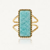 Bague dorée avec pierre rectangulaire bleu-vert veinée, sertie de petits points. Le corps de bague est double.