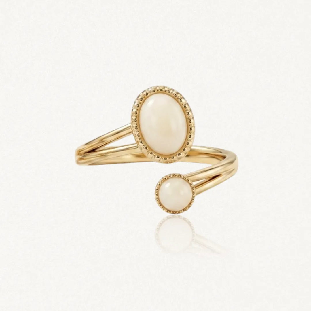 Bague ouverte dorée avec deux pierres cabochon crème, une ovale et une ronde, serties de bordures perlées.