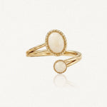 Bague ouverte dorée avec deux pierres cabochon crème, une ovale et une ronde, serties de bordures perlées.