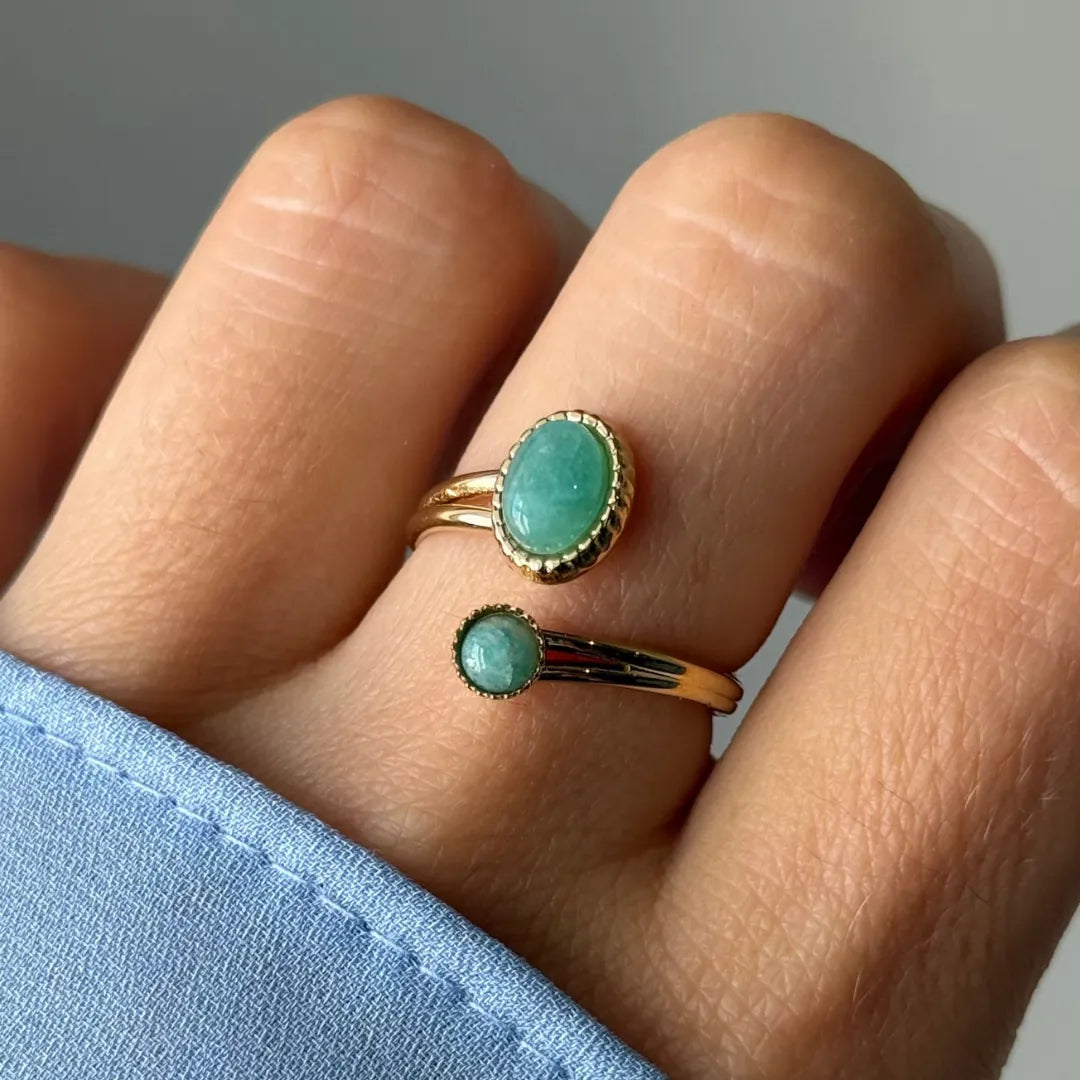 Main portant une bague dorée ouverte à deux pierres vert clair. Une grande ovale et une petite ronde, serties de détails