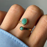 Main portant une bague dorée ouverte à deux pierres vert clair. Une grande ovale et une petite ronde, serties de détails