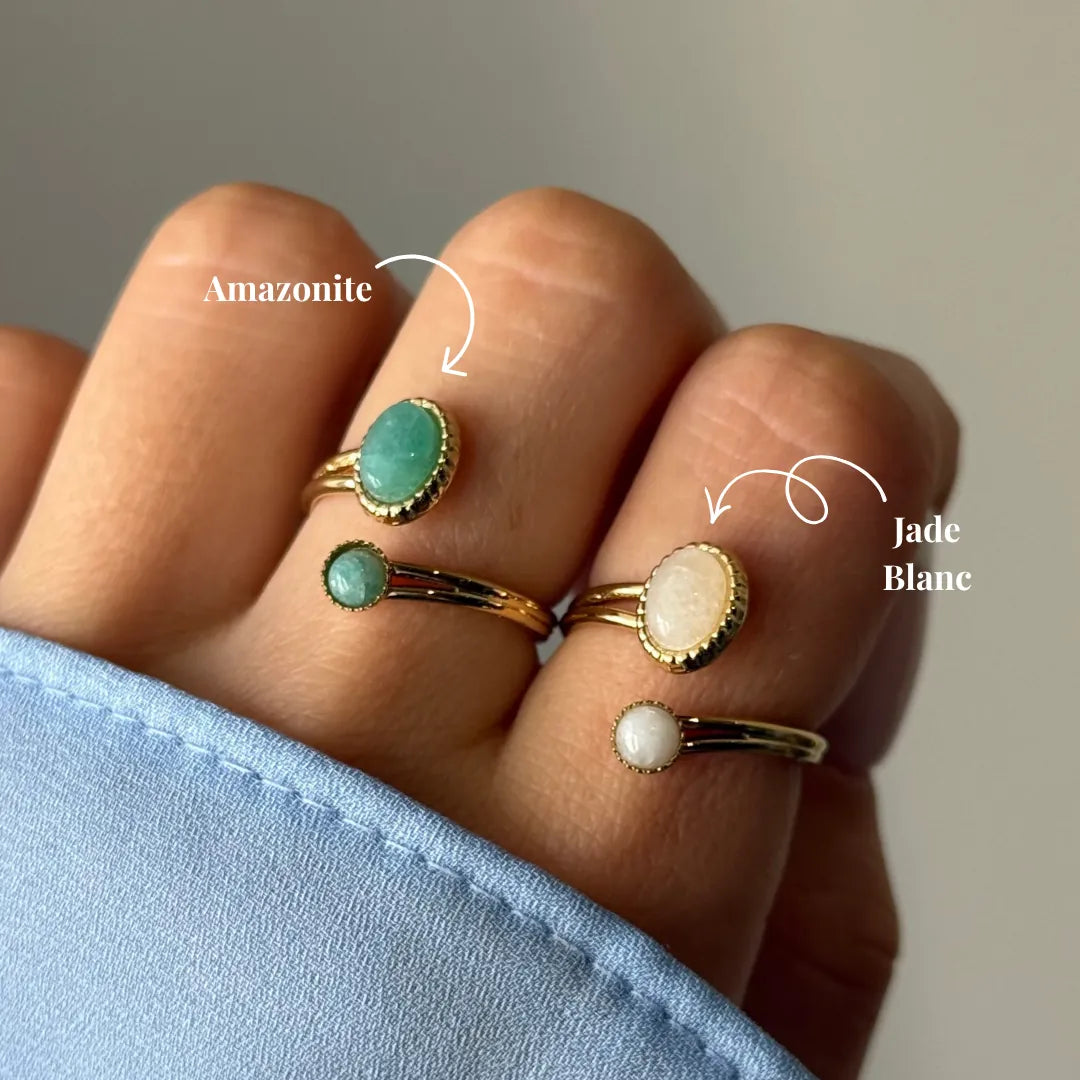 Quatre bagues dorées sur une main. Deux avec pierre ovale verte amazonite, deux avec pierre jade blanc ovale et ronde.