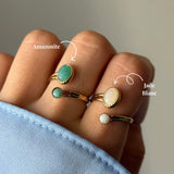 Quatre bagues dorées sur une main. Deux avec pierre ovale verte amazonite, deux avec pierre jade blanc ovale et ronde.