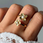 Bague ajustable en acier inoxydable doré, deux fleurs striées avec chacune une perle blanche. Portée sur un doigt.