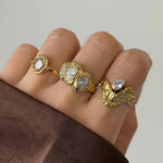 Bague Kendall en acier inoxydable doré avec strass en zirconium, portée avec d'autres bagues sur une main