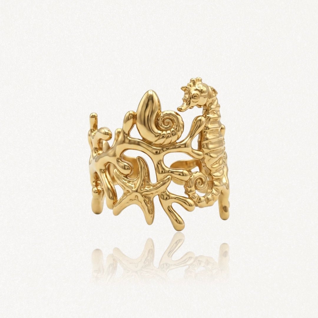 Bague en acier inoxydable doré, motif marin avec hippocampe, coquillage et étoiles de mer sur fond corallien.