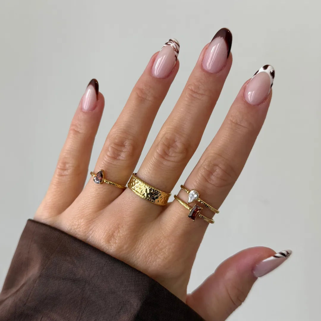 Main centrale : bague large en acier inoxydable doré à texture martelée portée sur un doigt avec d'autres bagues