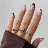 Bague Leandra en acier inoxydable doré avec un strass en zirconium bleu, portée sur un doigt avec manucure