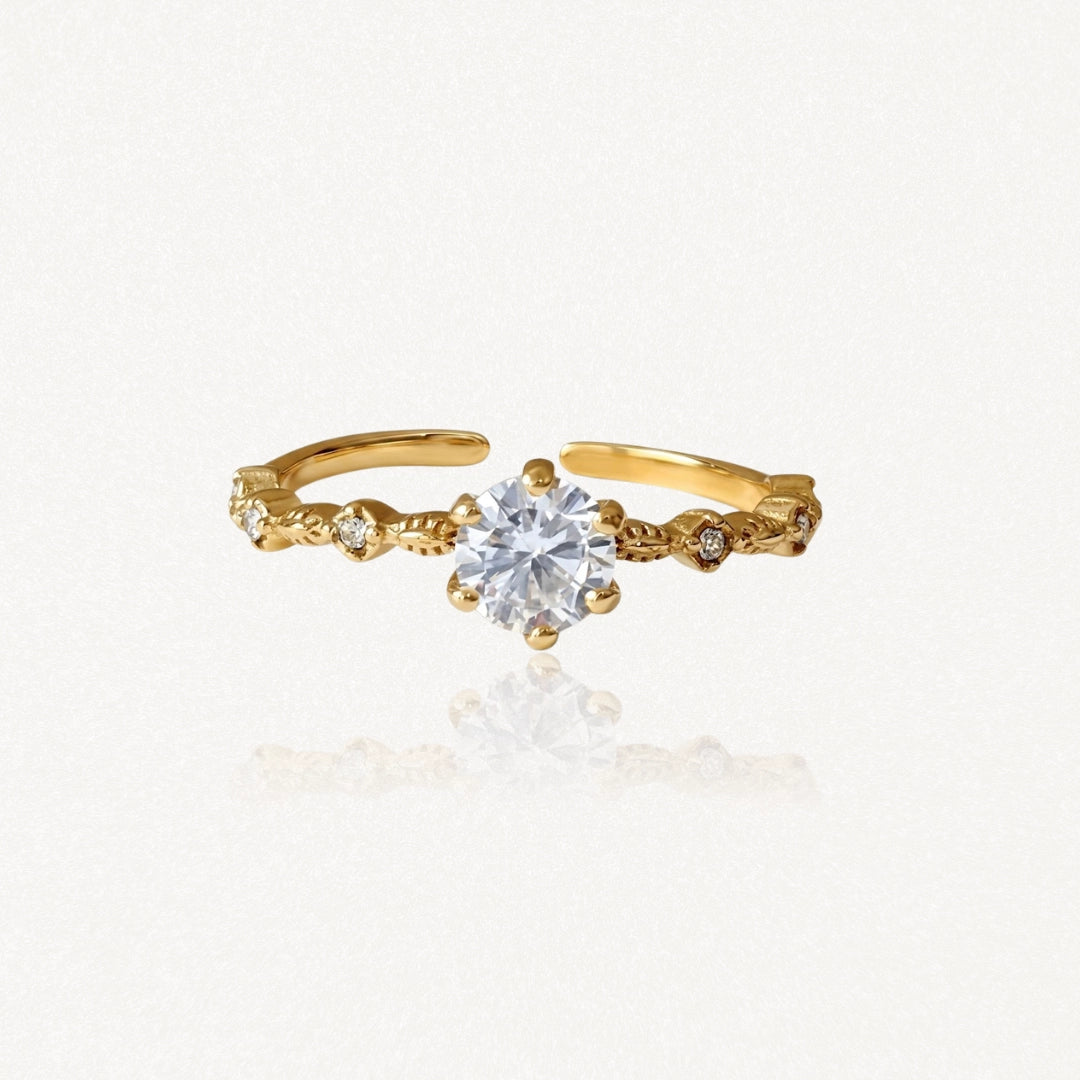 Bague ajustable en acier inoxydable doré avec solitaire central et petites pierres décoratives sur anneau ouvragé.