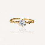 Bague ajustable en acier inoxydable doré avec solitaire central et petites pierres décoratives sur anneau ouvragé.