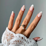 Bague ouverte en acier inoxydable doré, une fleur et une perle blanche à chaque extrémité, portée sur un doigt.