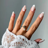 Bague ouverte en acier inoxydable doré, une fleur et une perle blanche à chaque extrémité, portée sur un doigt.