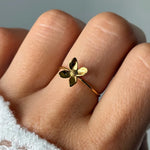 Bague en acier inoxydable doré, design fleur, portée sur un doigt. La fleur a quatre pétales et un centre texturé.