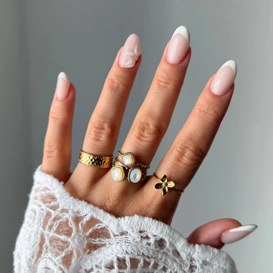 Main portant une bague ajustable fleur en acier inoxydable doré, avec des ongles manucurés et un vêtement en dentelle