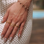 Bagues en acier inoxydable doré à motifs étoile de mer et coquillages, sur main de femme en robe blanche.