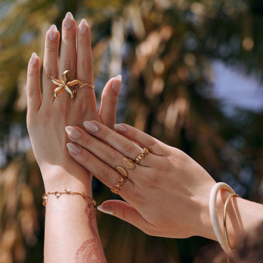 Grosse bague étoile de mer et bagues coquillage en acier inoxydable doré sur mains féminines manucurées.