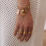 Bagues en acier inoxydable doré : coquillage, rangée de coquillages, pointes. Bracelet assorti sur main féminine.