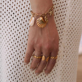 Bagues en acier inoxydable doré : coquillage, rangée de coquillages, pointes. Bracelet assorti sur main féminine.