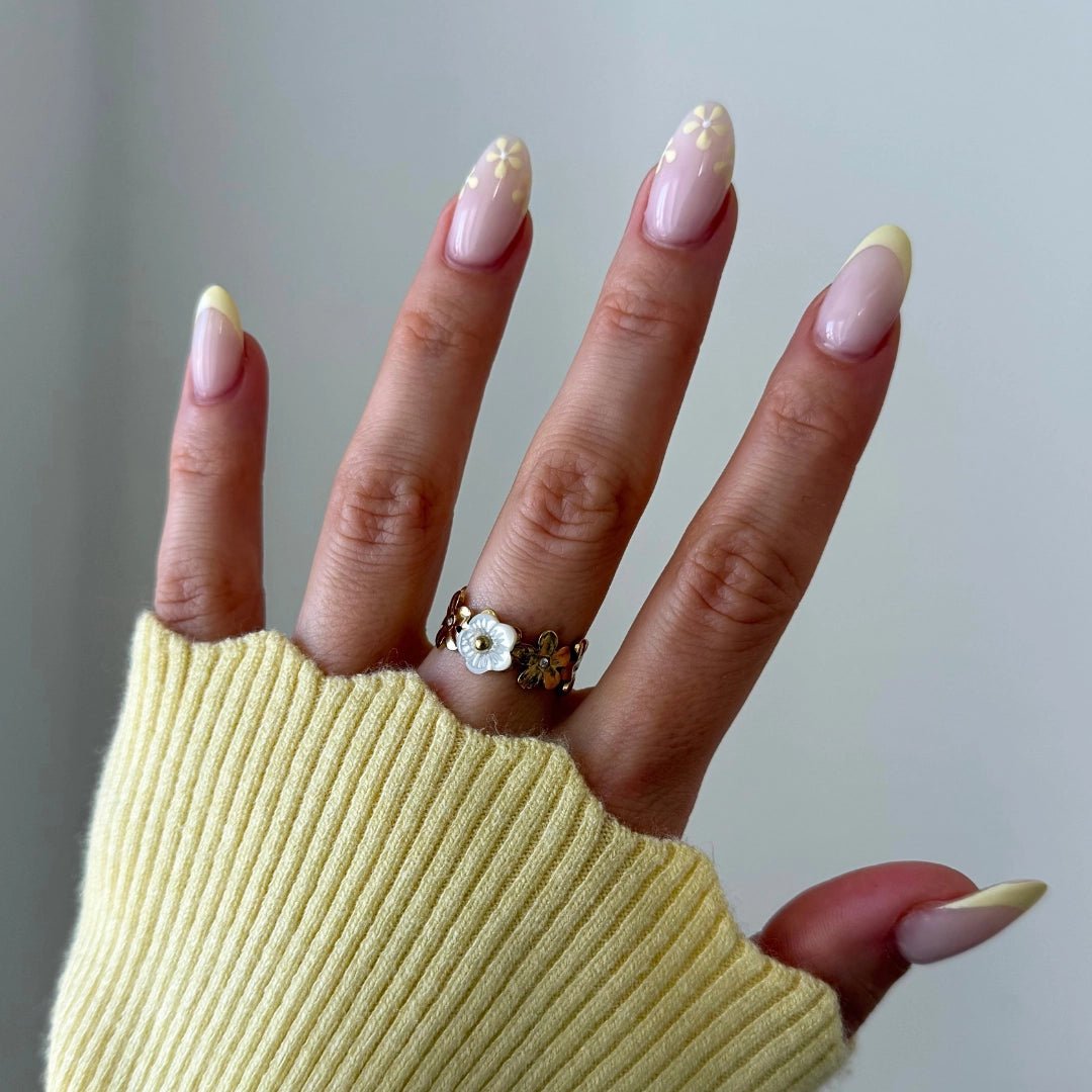 Bague femme en acier inoxydable doré motif floral: une fleur nacre, deux dorées. Portée main aux ongles french manucure