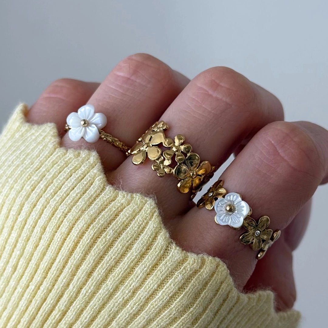 Bagues fleuries en acier inoxydable doré: fleurs nacre, fleurs dorées entrelacées, et fleurs nacre avec strass.