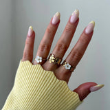 Trois bagues en acier inoxydable doré à motifs floraux (nacre et métal) sur une main en pull jaune.