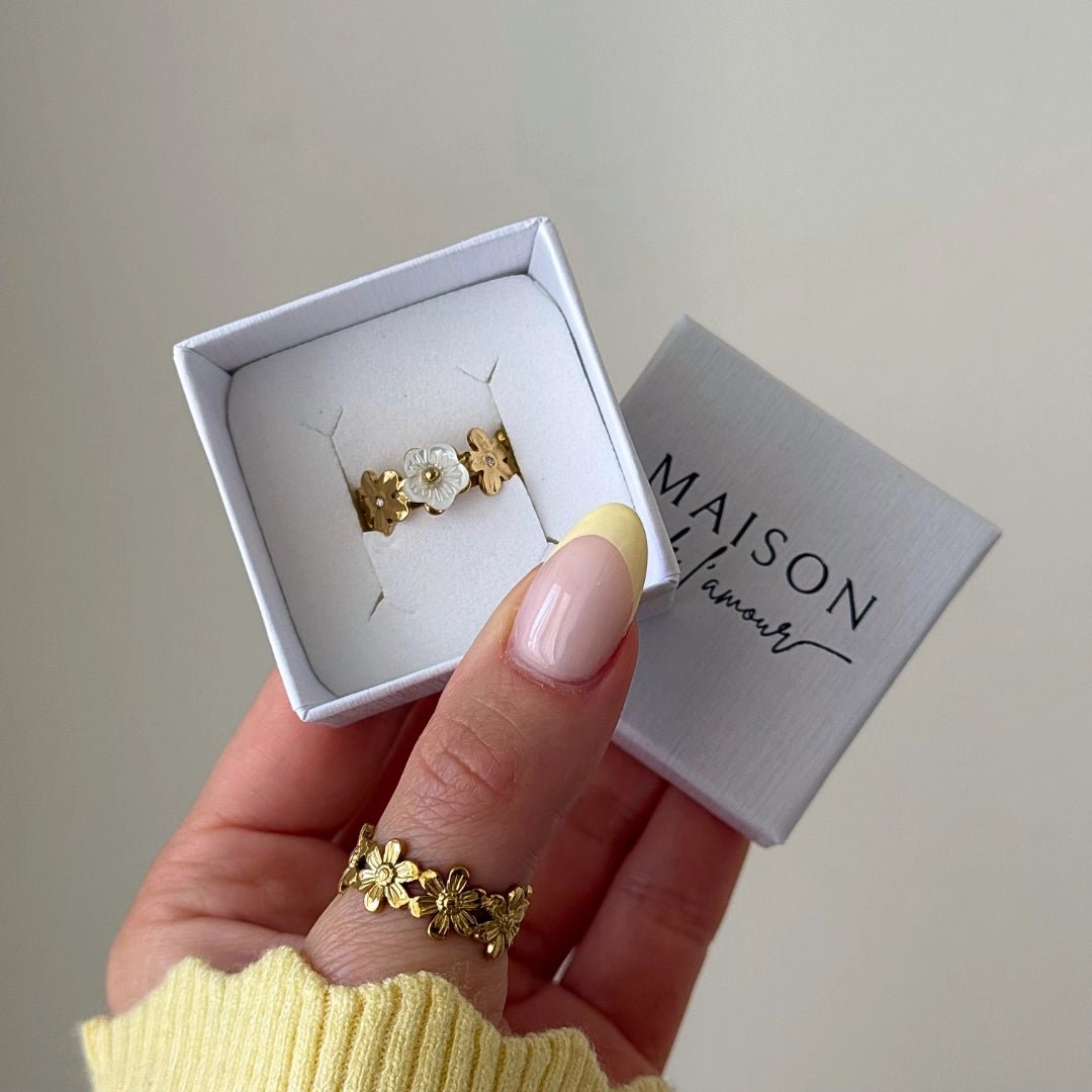 Bague en acier inoxydable dorée à motifs de fleurs et nacre en boîte, une autre bague florale portée au pouce.